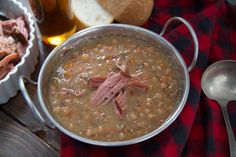 a bowl of soup with meat and beans next to bread on a red checkered table cloth