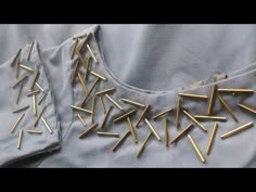 some gold pins are laying on top of a gray shirt with holes in the back