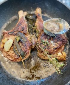 two pieces of meat in a frying pan with a spoon on the side and some herbs sprinkled on top