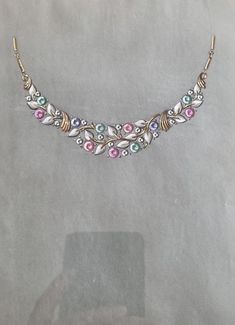 This original gouache, created in the 1930s by a New York jeweler, is a rare and unique illustration designed as a prototype for an exceptional jewelry piece. The artwork depicts a floral necklace with finely detailed motifs, featuring golden leaves and pastel-colored gemstones (pink, green, blue), reflecting the refined style of Art Deco. This prototype highlights a high level of artisanal craftsmanship, showcasing the harmonious combination of floral elements and precious stones. The gouache i Floral Necklace, New Yorker, Gemstone Colors, Vintage Charms, Gold Frame, Patina, Precious Stones, Fashion Art, Jewelry Pieces