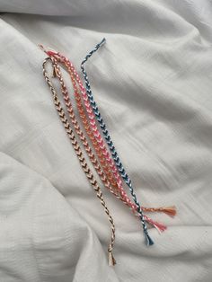 three tasseled necklaces laying on top of a white bed sheet with blue, pink and orange beads