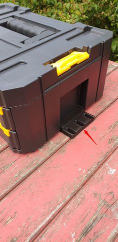 a large black box sitting on top of a wooden table next to bushes and shrubbery