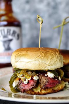 a steak sandwich with pickles and cheese on a plate next to a bottle of beer