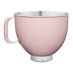 a pink coffee cup sitting on top of a white table next to a metal bowl