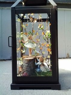 a glass box with flowers and fairy figurines inside