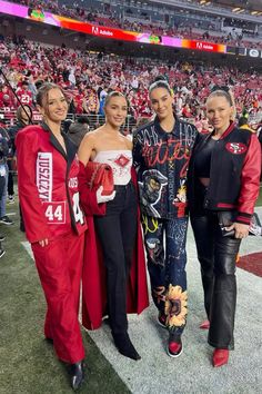 three women in red and black outfits standing on the field at a football game with fans