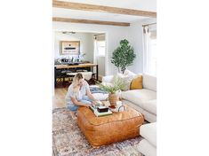 a woman sitting on top of a brown ottoman in a living room