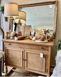 a wooden dresser topped with lots of vases next to a large mirror and lamp