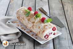 a white plate topped with a roll covered in cream and raspberries next to a knife