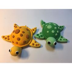 two plastic sea animals sitting next to each other on a white counter top with one green turtle and the other yellow turtle