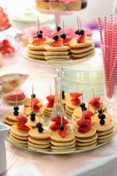 some pancakes and berries are on a table with other desserts in the back ground