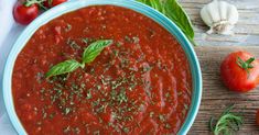 a blue bowl filled with tomato sauce next to fresh tomatoes and garlic on a wooden table