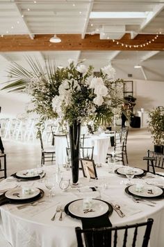 a table is set with black and white place settings, flowers in a tall vase