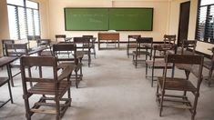 an empty classroom with wooden chairs and green chalkboards on the wall, in front of two large windows