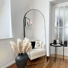 a living room with white walls and wood floors, a black vase filled with pamodia