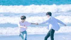 two people holding hands while walking on the beach near the ocean with waves in the background