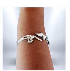 a woman's arm wearing a silver bracelet with two small dogs on the wrist