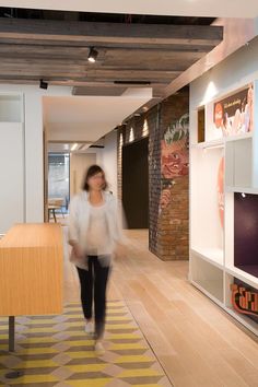 a woman is walking down the hallway in an office with yellow and white rugs