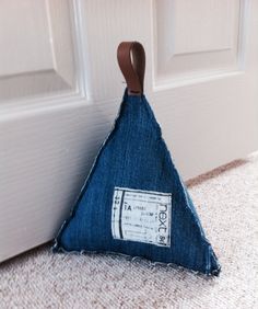 a small triangle shaped object made out of blue jeans sitting on the floor next to a door