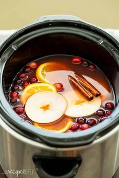 apples, cinnamon and orange slices in a crock pot filled with liquid to make an apple cider