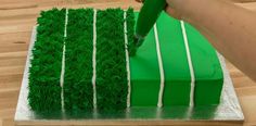 a person cutting into a green cake with white stripes on the side and grass in the middle