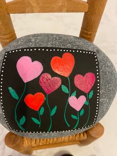 a painted rock with hearts and flowers on it sitting on top of a wooden chair