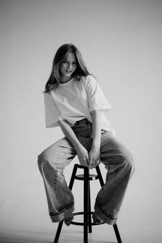 a woman sitting on top of a stool posing for a photo in black and white