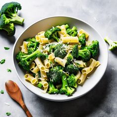 a bowl filled with pasta and broccoli on top of a table next to a wooden spoon