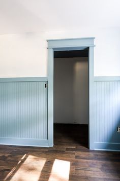 an empty room with wooden floors and blue painted walls, open door to another room