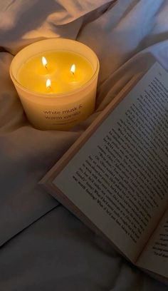 an open book sitting on top of a bed next to a lit candle