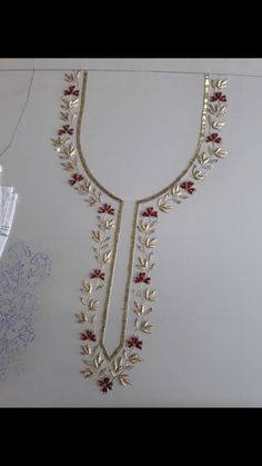 a gold necklace with red stones and leaves on the bottom is hanging from a white wall