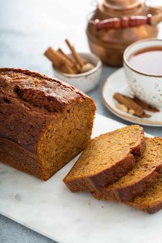 sliced loaf of pumpkin spice bread on a cutting board with cinnamon sticks and tea in the background