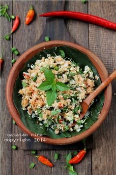 a wooden bowl filled with rice and vegetables on top of a table next to chili peppers