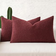 two red pillows sitting on top of a white couch next to a green cactus plant