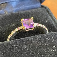 an engagement ring with pink and yellow sapphires in a black box on top of a wooden table