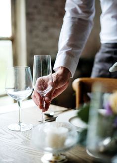 a person is holding a wine glass at a table with two empty wine glasses on it