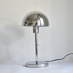 a lamp that is sitting on top of a table next to a white wall with a black cord