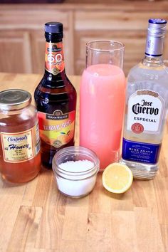 the ingredients to make an alcoholic drink are displayed on a wooden counter top, including orange juice, lemonade, and ginger syrup