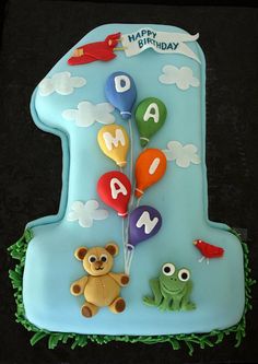 a blue birthday cake with an animal and balloons on it's number one candle