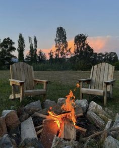 two wooden chairs sitting next to a fire pit on top of a grass covered field