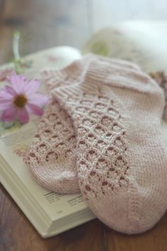 a pair of pink knitted socks sitting on top of a book next to a flower