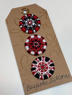 three red, white and black buttons sitting on top of a brown paper bag tag