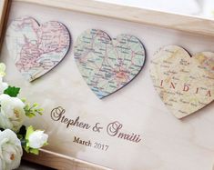 three heart shaped maps in a wooden frame with flowers on the table next to it