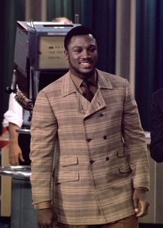 a man in a suit and tie standing next to a tv set with other people behind him