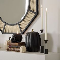 a white mantle topped with books and a black pumpkin next to a mirror on top of it