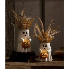 two halloween decorations made to look like ghostes with pumpkins in their hands, sitting on a table