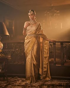 a woman in a gold sari standing on a balcony with her hands on her hips