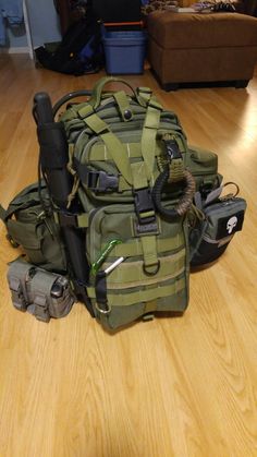 a large green backpack sitting on top of a wooden floor next to other bags and tools