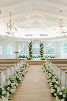 an aisle lined with white flowers and greenery in front of a church pews