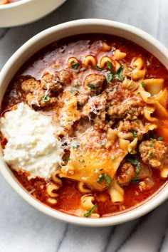 two bowls of pasta and meat soup on a marble counter top, one with sour cream